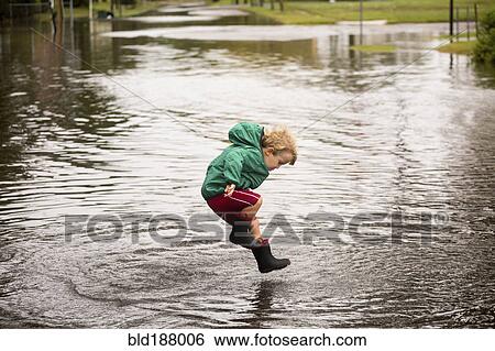 Stock Photograph - Caucasian boy jumping in puddle. Fotosearch