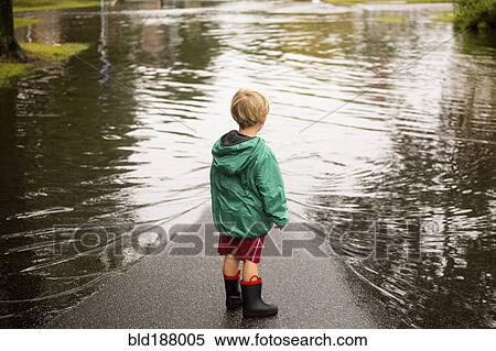 Stock Photography - Caucasian boy wearing puddles near flood. Fotosearch