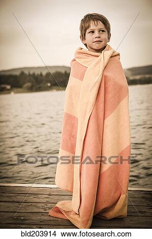 Picture - Caucasian boy wrapped in towel on wooden dock. Fotosearch