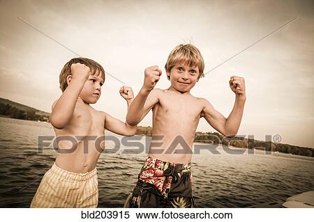 Stock Photography - Caucasian boys flexing muscles on wooden dock. Fotosearch