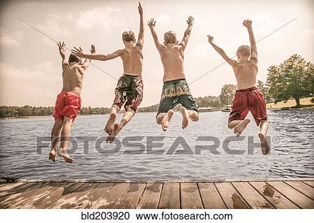Stock Image - Caucasian boys jumping off wooden dock. Fotosearch