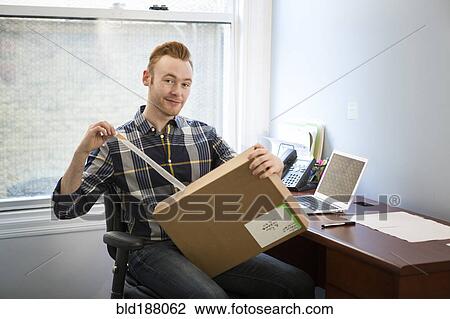 Stock Image - Caucasian businessman opening package in office. Fotosearch