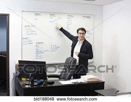Stock Photo - Caucasian businessman pointing to whiteboard in office. Fotosearch