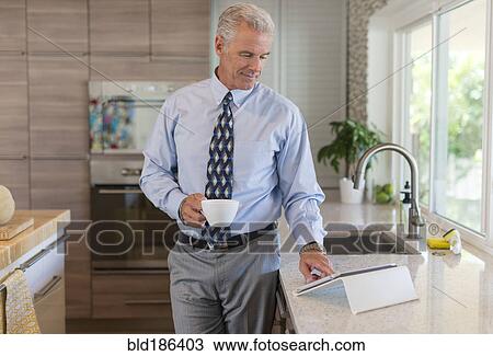 Stock Image - Caucasian businessman using digital tablet in kitchen. Fotosearch