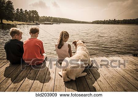 Caucasian children sitting on wooden dock with dog View Large Photo Image Stock Photo - Caucasian children sitting on wooden dock with dog. Fotosearch