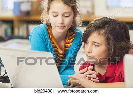 Stock Image - Caucasian children using laptop in library. Fotosearch