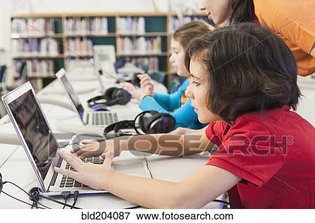 Stock Photo - Caucasian children using laptops in library. Fotosearch