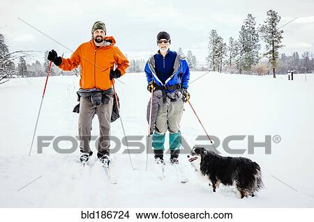 Picture - Caucasian couple and dog cross-country skiing in snowy field. Fotosearch