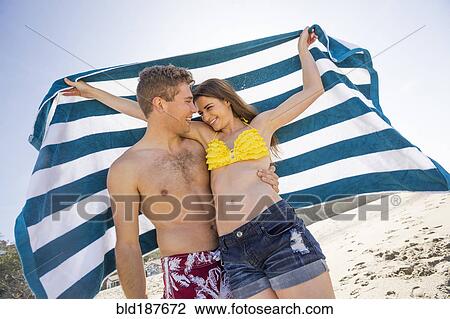 Stock Image - Caucasian couple holding towel on beach. Fotosearch