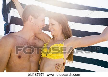 Stock Image - Caucasian couple hugging under towel. Fotosearch