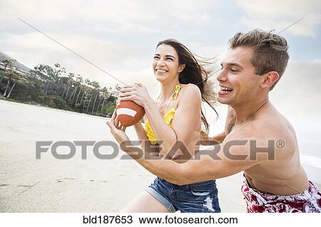 Stock Image - Caucasian couple playing on beach. Fotosearch