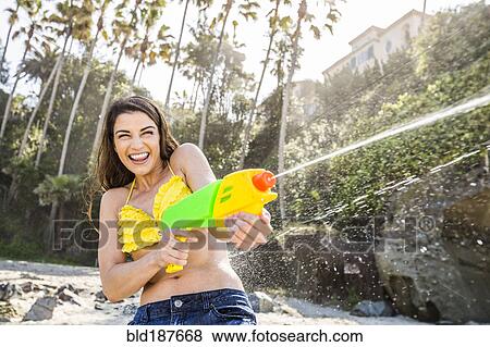 Stock Photo - Caucasian couple playing with squirt guns on beach. Fotosearch