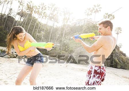 Stock Photograph - Caucasian couple playing with squirt guns on beach. Fotosearch