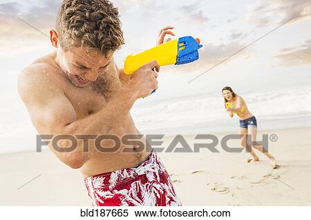 Stock Photography - Caucasian couple playing with squirt guns on beach. Fotosearch