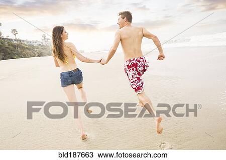 Stock Image - Caucasian couple running on beach. Fotosearch