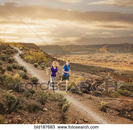 Stock Image - Caucasian couple running on remote dirt path. Fotosearch