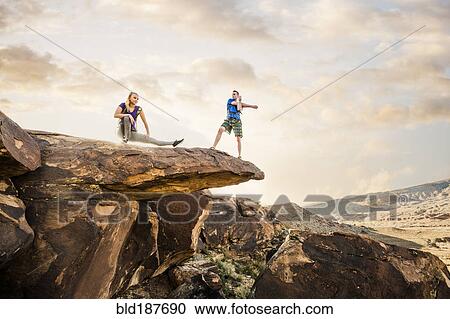 Stock Image - Caucasian couple stretching on rock formation. Fotosearch