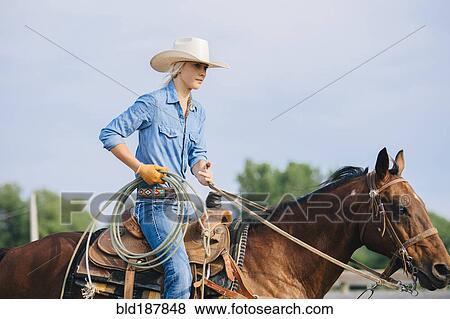 Stock Photo - Caucasian cowgirl holding lasso on horseback. Fotosearch