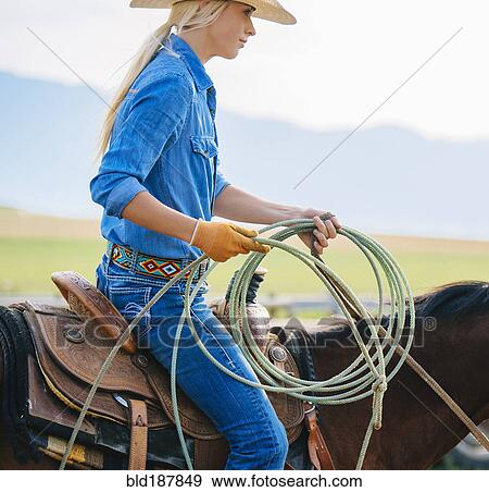 Stock Photo - Caucasian cowgirl holding lasso on horseback. Fotosearch