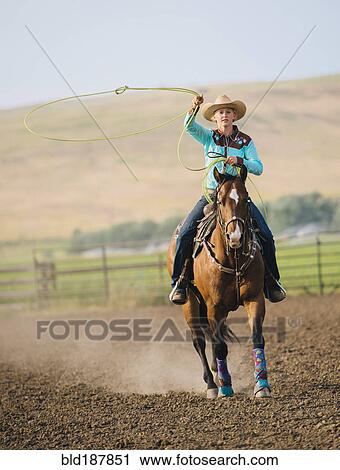 Stock Image - Caucasian cowgirl throwing lasso on horseback. Fotosearch