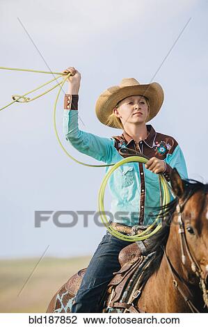 Stock Image - Caucasian cowgirl throwing lasso on horseback. Fotosearch