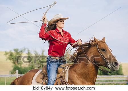 Stock Photo - Caucasian cowgirl throwing lasso on horseback. Fotosearch