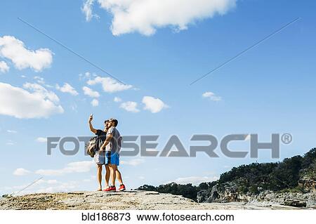 Stock Image - Caucasian friends taking selfie on hilltop. Fotosearch