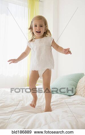 Stock Photo - Caucasian girl jumping on bed. Fotosearch