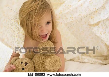 Stock Image - Caucasian girl playing with teddy bear under blankets. Fotosearch