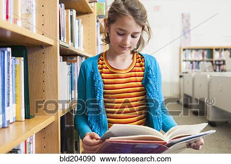 Stock Image - Caucasian girl reading book in library. Fotosearch