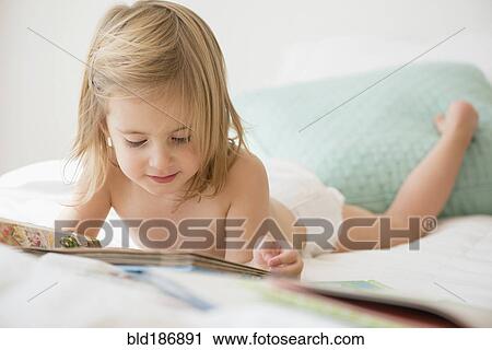 Stock Image - Caucasian girl reading book on bed. Fotosearch