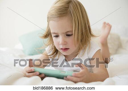 Caucasian girl using cell phone on bed View Large Photo Image Stock Photograph - Caucasian girl using cell phone on bed. Fotosearch
