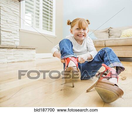 Stock Image - Caucasian girl wearing adult shoes in living room. Fotosearch