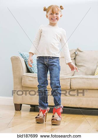 Stock Photo - Caucasian girl wearing adult shoes in living room. Fotosearch