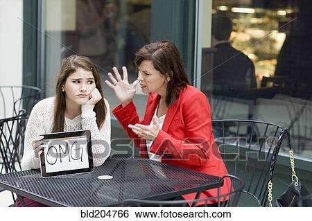 Stock Photograph - Caucasian girl with tablet as mother chastises her at cafe. Fotosearch