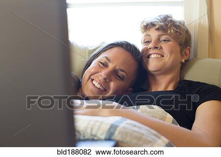 Stock Image - Caucasian lesbian couple cuddling in bed. Fotosearch