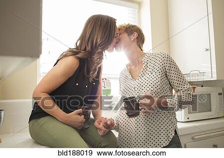 Stock Photo - Caucasian lesbian couple kissing in kitchen. Fotosearch