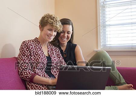 Stock Photo - Caucasian lesbian couple using laptop on sofa. Fotosearch