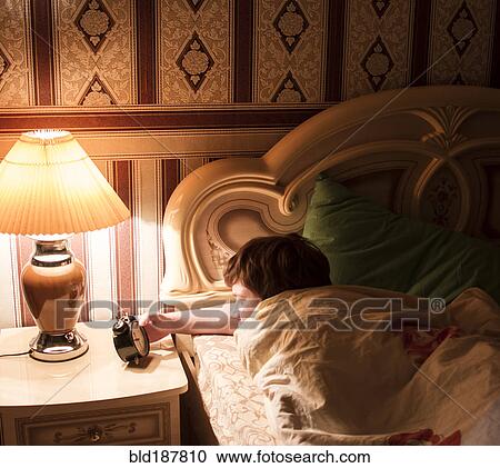 Caucasian man checking alarm clock in bed View Large Photo Image Stock Image - Caucasian man checking alarm clock in bed. Fotosearch