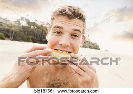 Stock Image - Caucasian man eating fruit on beach. Fotosearch