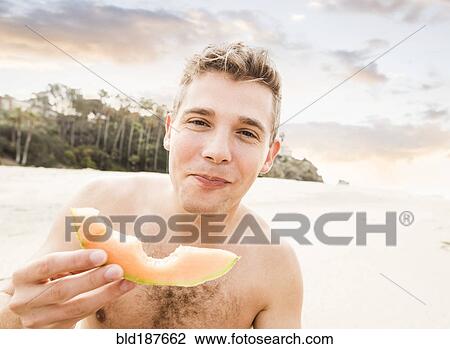 Caucasian man eating fruit on beach View Large Photo Image Stock Image - Caucasian man eating fruit on beach. Fotosearch