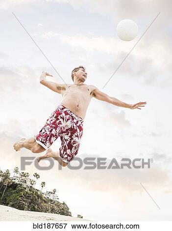 Stock Photo - Caucasian man hitting volleyball on beach. Fotosearch
