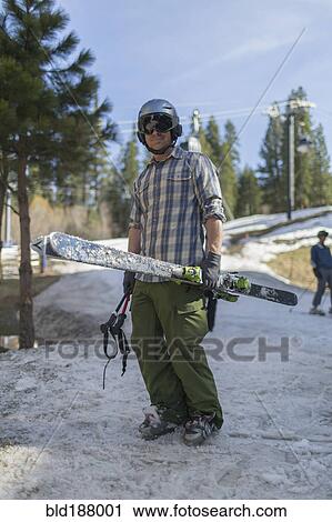 Stock Image - Caucasian man holding skis on snowy hillside. Fotosearch