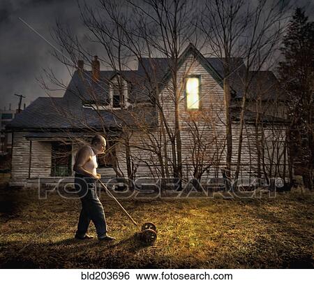 Stock Photograph - Caucasian man mowing lawn outside home. Fotosearch