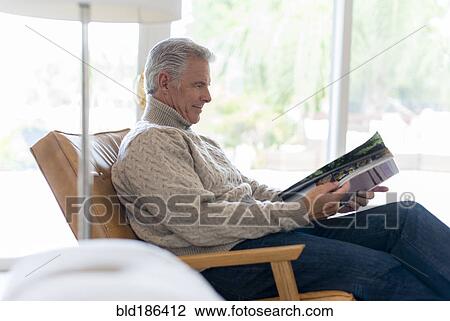 Stock Image - Caucasian man reading magazine in armchair. Fotosearch