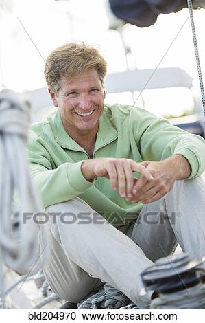 Stock Image - Caucasian man sitting on sailboat. Fotosearch