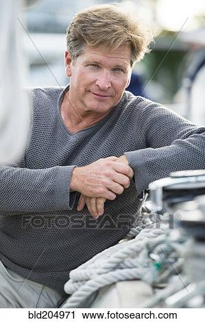 Stock Image - Caucasian man sitting on sailboat. Fotosearch