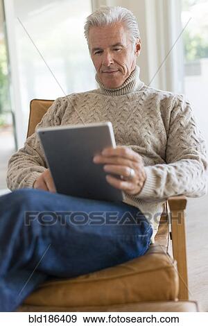 Stock Photo - Caucasian man using digital tablet in armchair. Fotosearch