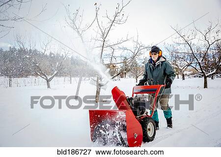 Stock Photo - Caucasian man using snow blower in snowy field. Fotosearch