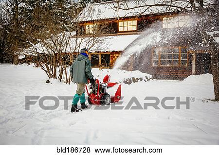 Stock Photo - Caucasian man using snow blower in snowy driveway. Fotosearch
